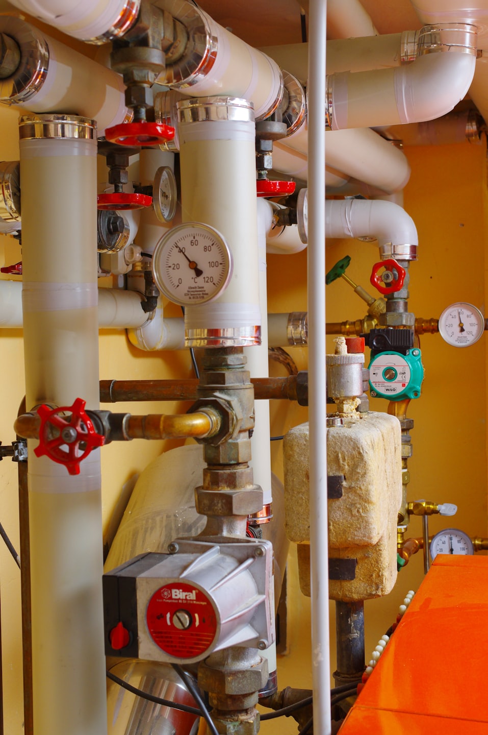 Beige insulated pipes and brass fittings in a utility room.