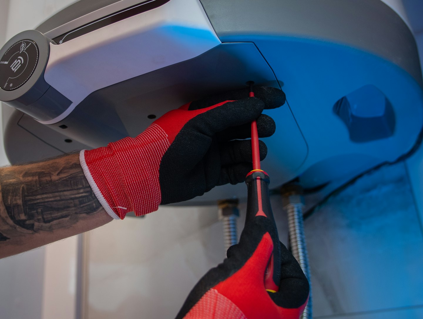 Hands in work gloves tighten a screw on a water heater.