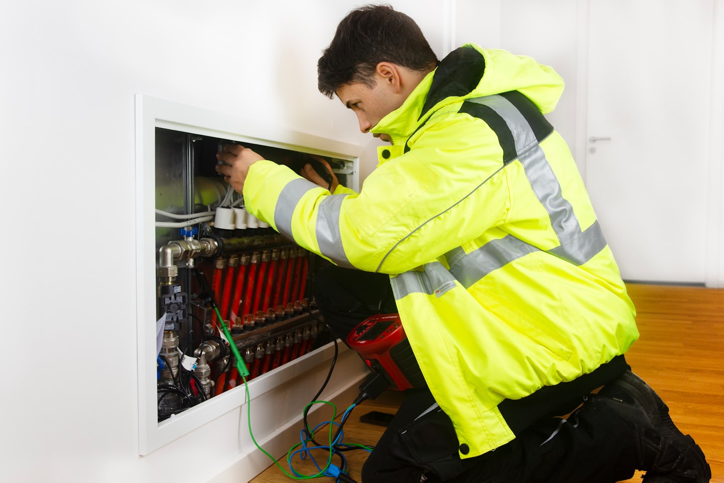 Technician in yellow jacket works on underfloor heating system.
